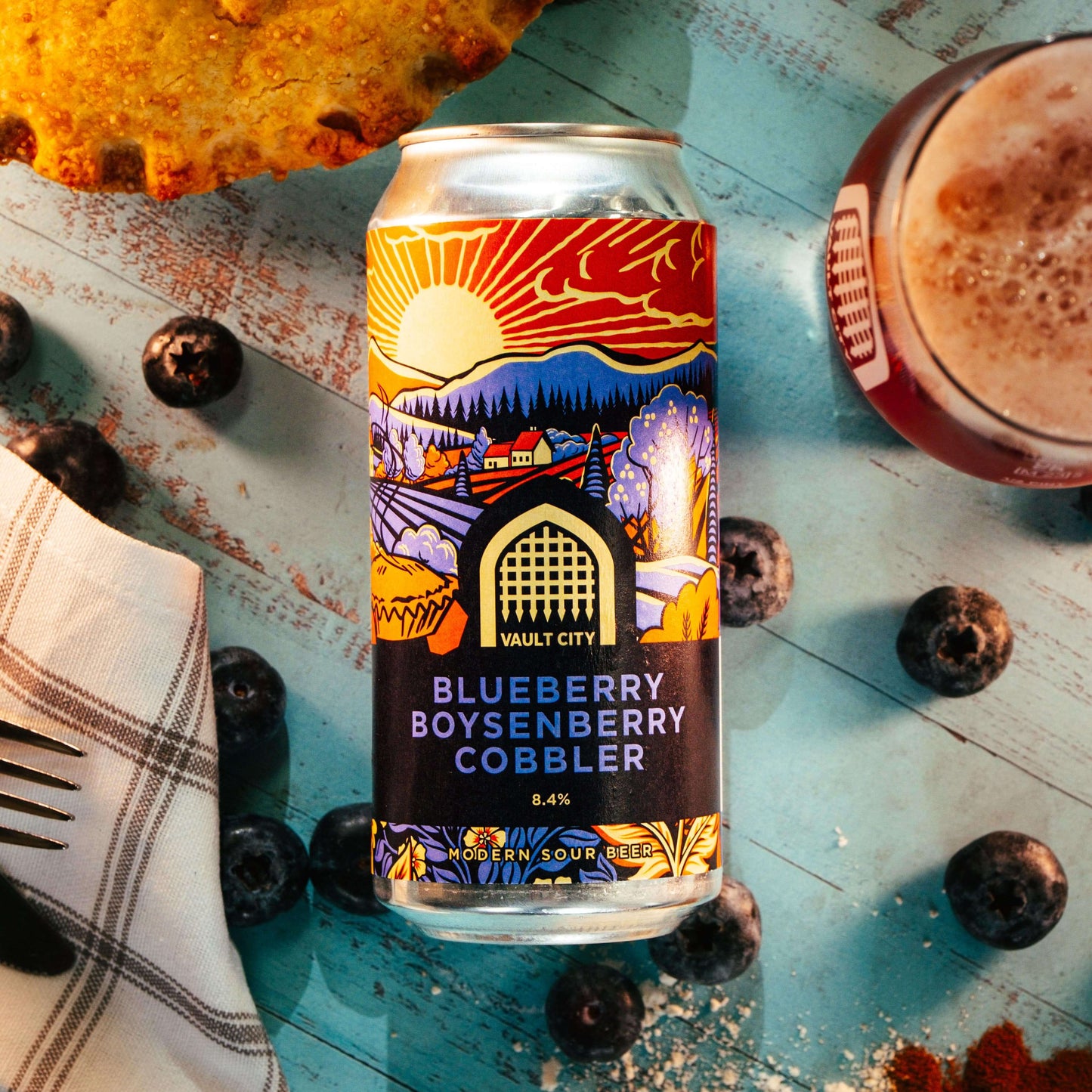 Blueberry Boysenberry Cobbler pastry sour beer can surrounded by fresh blueberries and pie on a rustic wooden table.