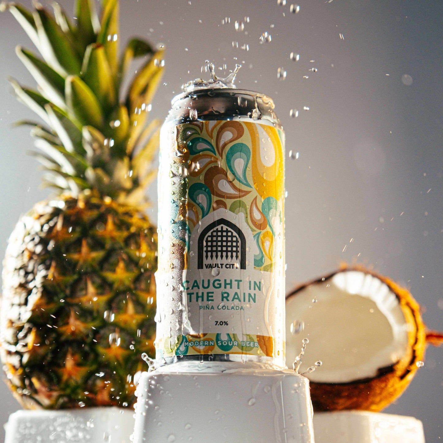 "Caught in the Rain - Pina Colada sour beer can with splashes, pineapple and coconut in the background"