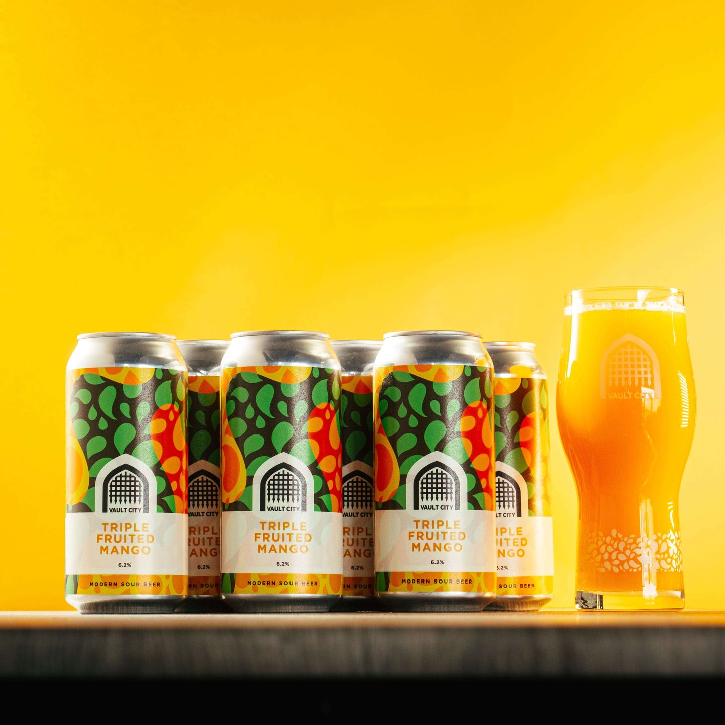 6-Pack Triple Fruited Mango session sour beer cans and a full glass, showcasing vibrant label and rich mango color against a yellow background.