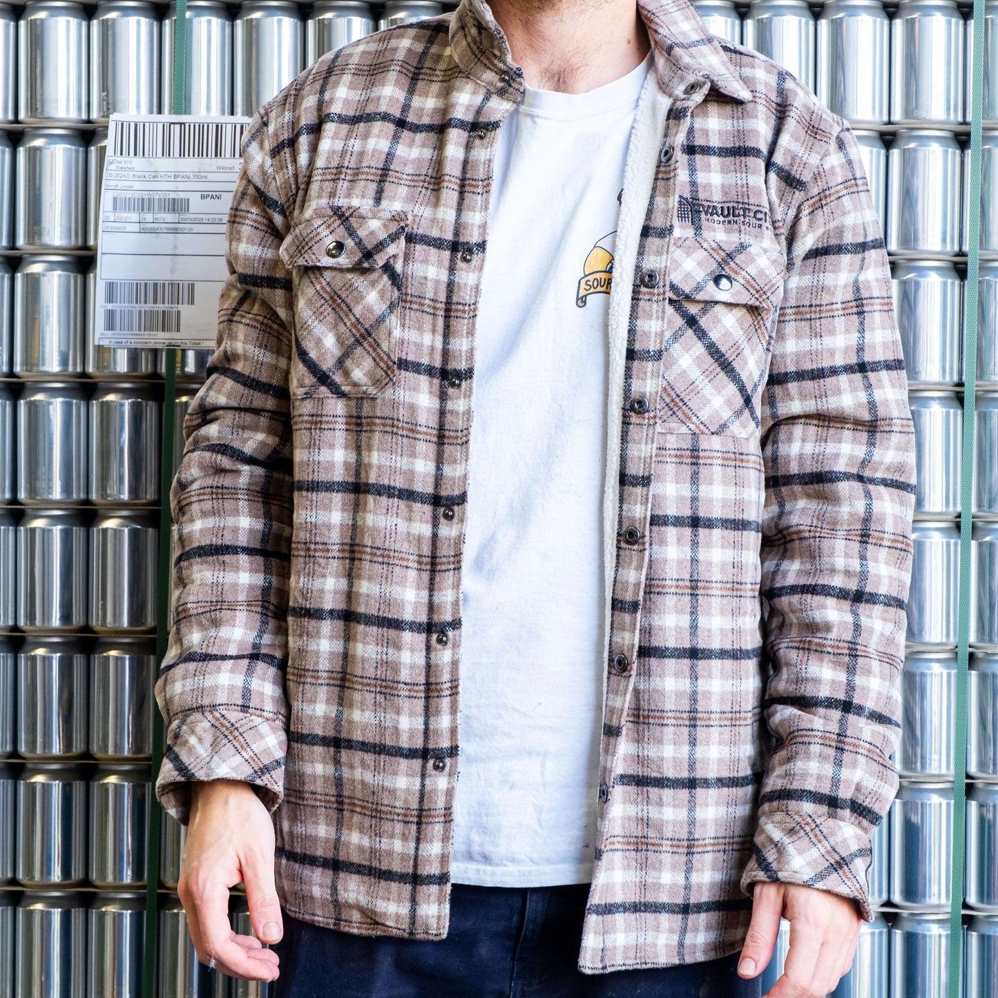 Vault City fleece-lined jacket in grey check, featuring embroidered logo, worn by person in front of metallic background