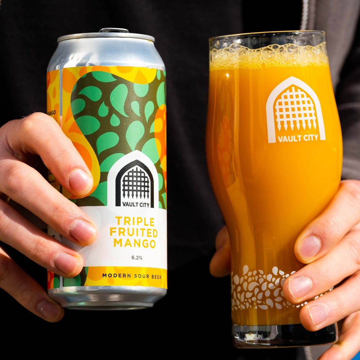 Person holding a can and glass of Triple Fruited Mango modern sour beer by Vault City, featuring rich Alphonso mango flavors, 6.2% ABV, 440ml.