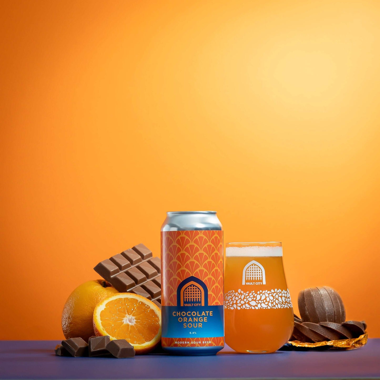 Can and glass of Chocolate Orange Sour surrounded by chocolate pieces and orange slices against an orange background.