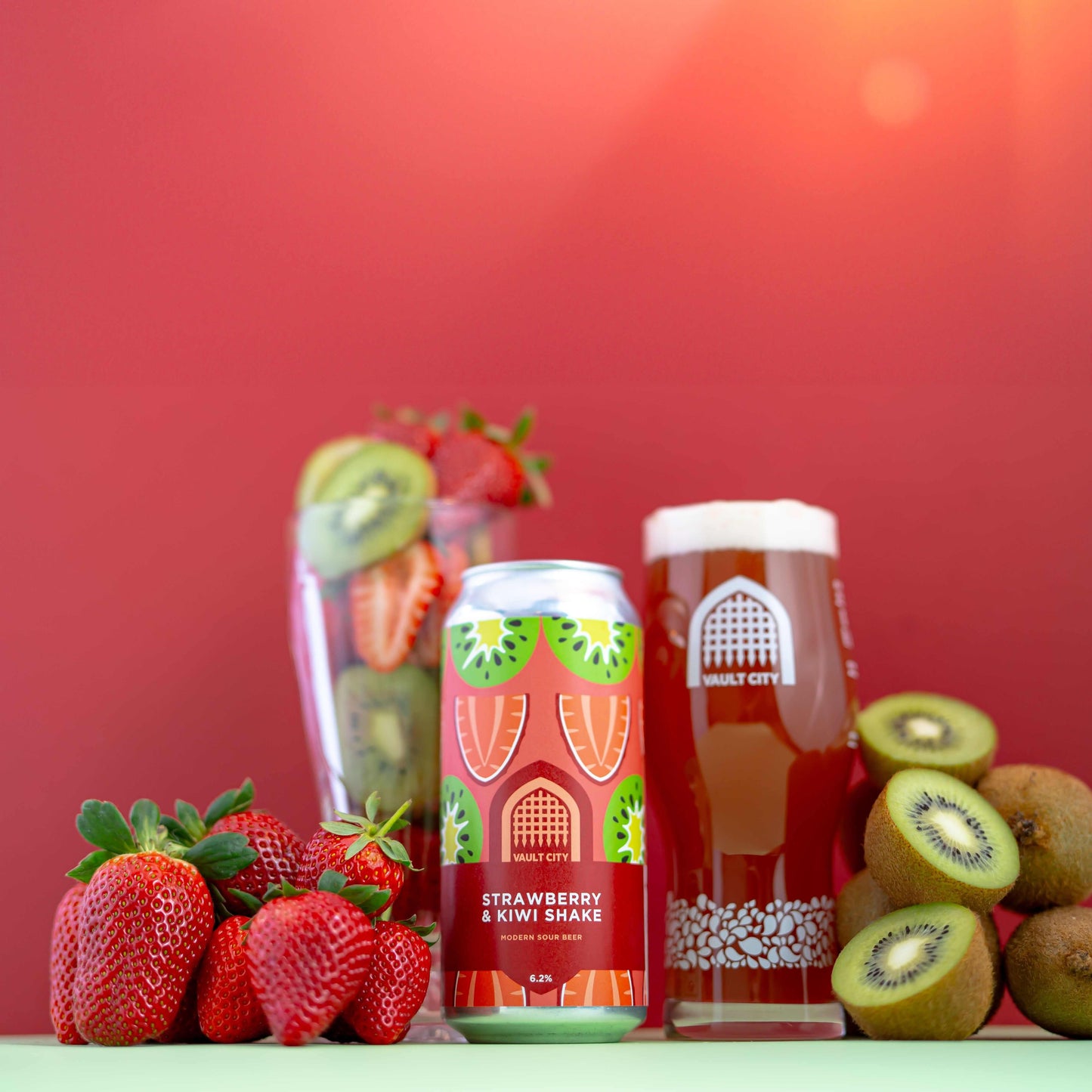 Strawberry & Kiwi Shake can with fresh strawberries and kiwis, next to a glass of fruity shake against a red background.