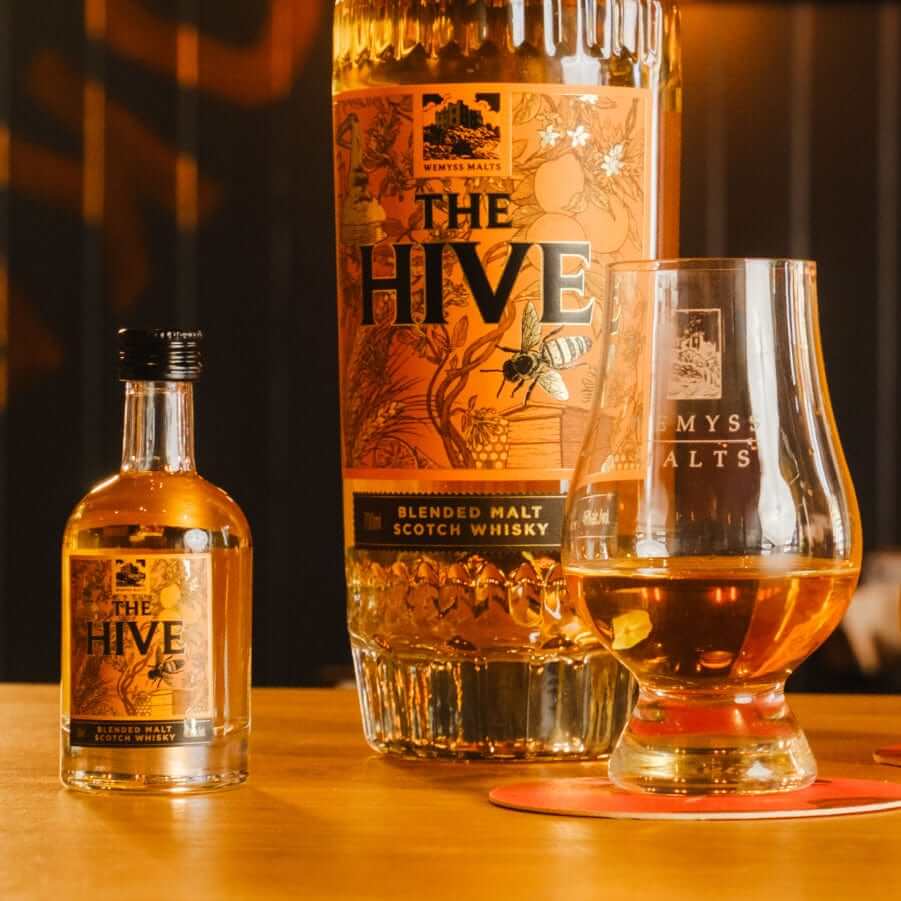 The Hive Wemyss Malts 5ml miniature Scotch whisky bottle and glass on a wooden table