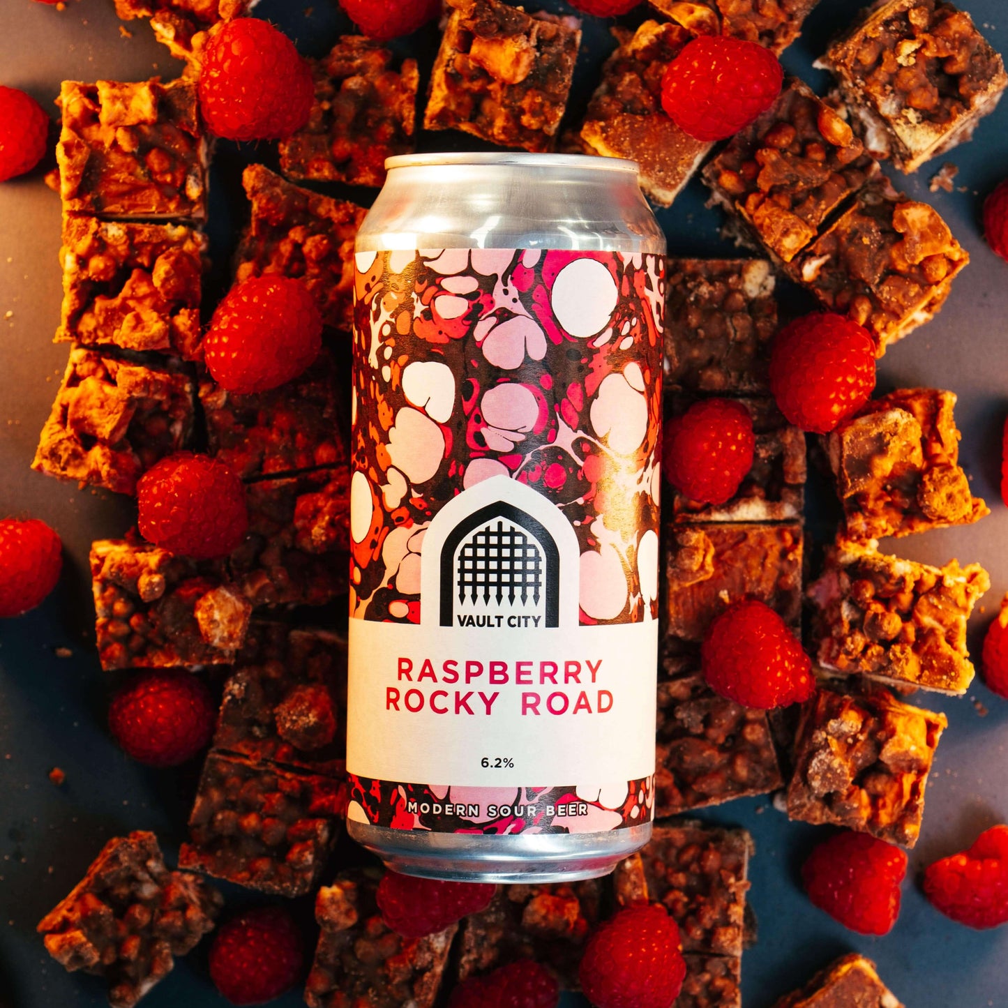 Raspberry Rocky Road dessert sour beer can surrounded by squares of rocky road and fresh raspberries.
