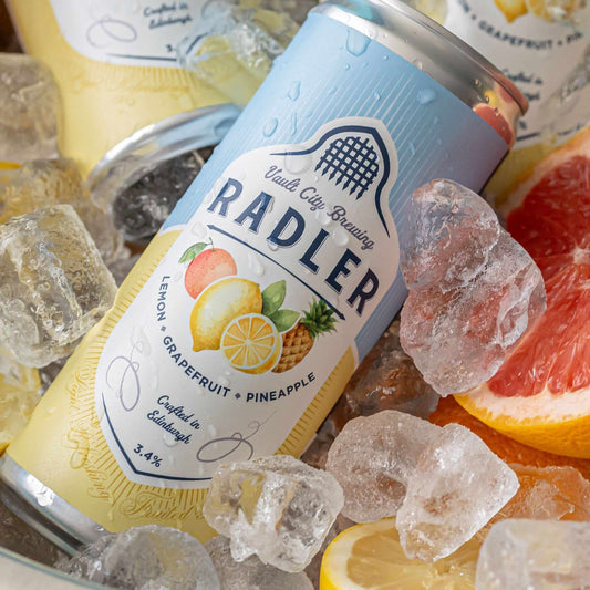 Can of Vault City Brewing Radler with lemon, grapefruit, and pineapple flavor on ice with fresh fruit slices.