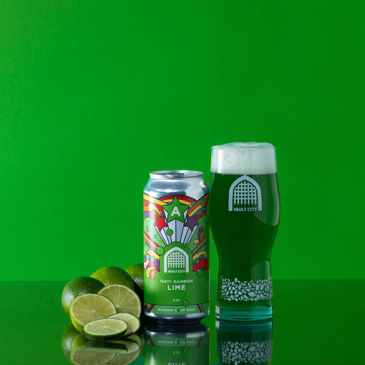 Tasty Rainbow Lime sour drink can and glass with fresh limes on a vibrant green background.