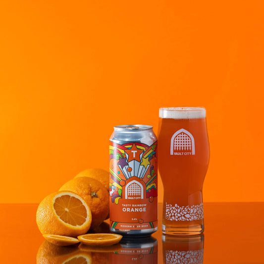 Tasty Rainbow Orange beer can and glass with fresh orange slices in vibrant orange background.