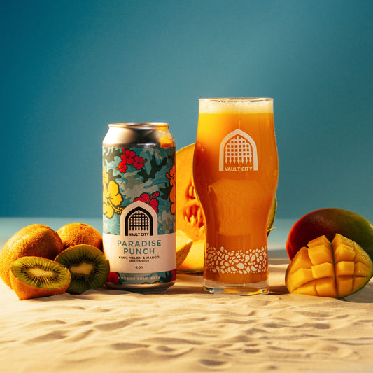 Paradise Punch Kiwi Melon Mango Session Sour beer can and glass with fresh kiwi, melon, and mango fruit on a sunny beach.